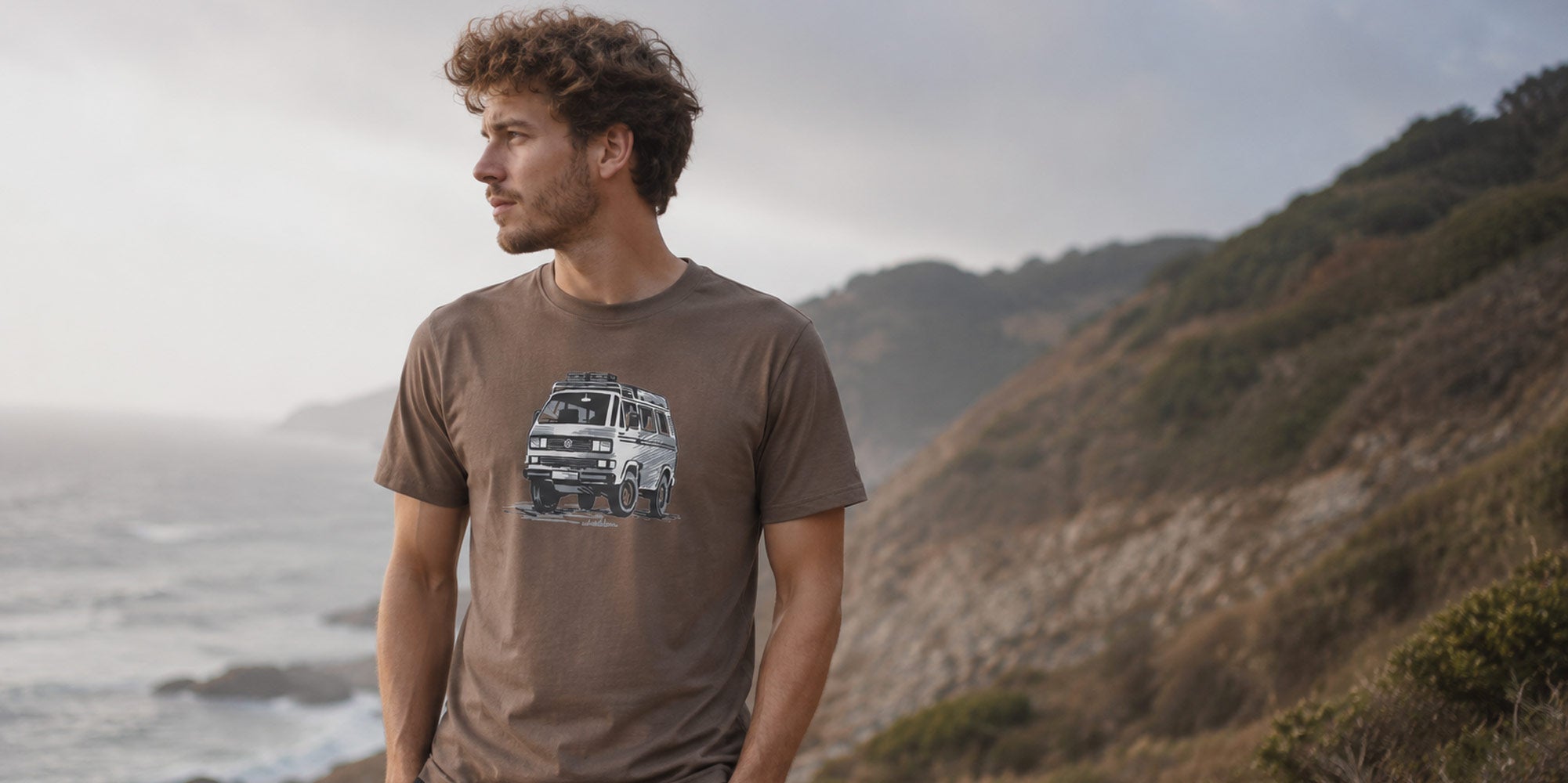 Mann mit VW-Bulli T-Shirt steht an einem Küstenrand